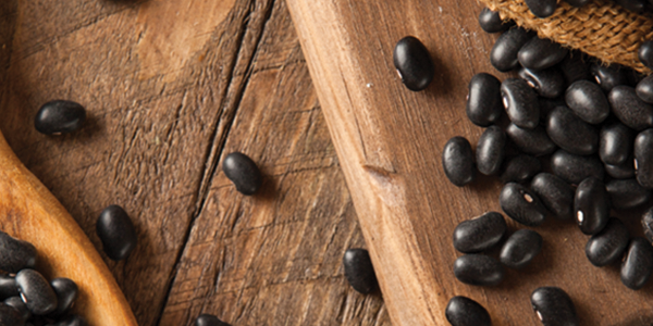 blackbeans_0 A wooden spoon filled with black beans on top of a table