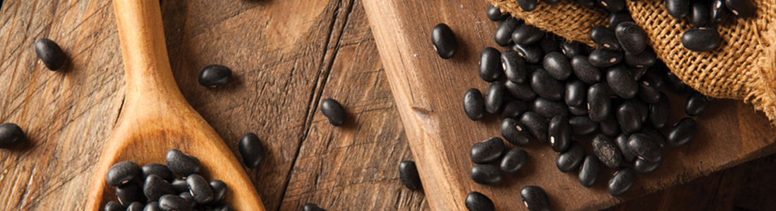 blackbeans_0 A wooden spoon filled with black beans on top of a table