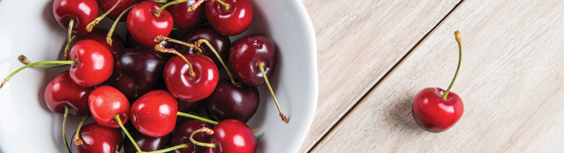 cherries A white bowl filled with cherries on top of a wooden table