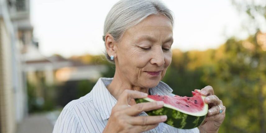 An older woman eating a piece of watermelon